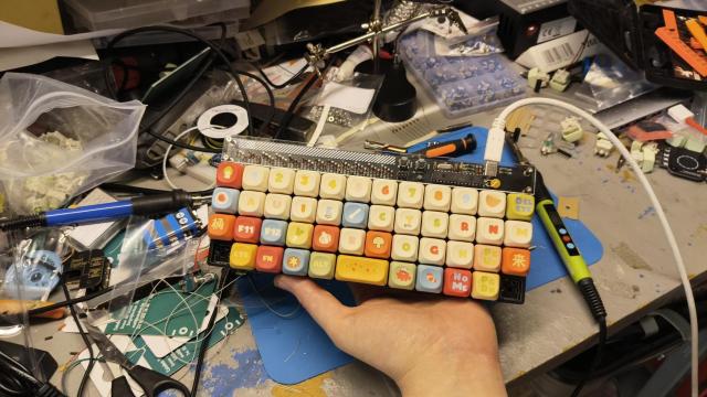 12x4 ortho keyboard, model "plaid" by 42keebs.eu, with cute keycaps in beige with some keys red, blue, orange, green or yellow. Some keys have illustrations instead of letter labels (a leek, a mushroom, a cabbage leaf, an octopus, ...)