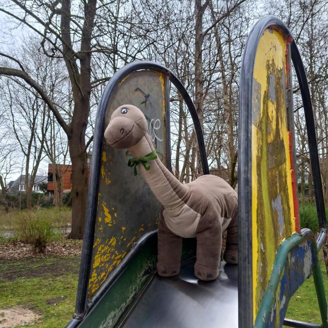 Ein Brontosaurier mit karierter Schleife um den langen Hals auf einer Rutsche im Park.