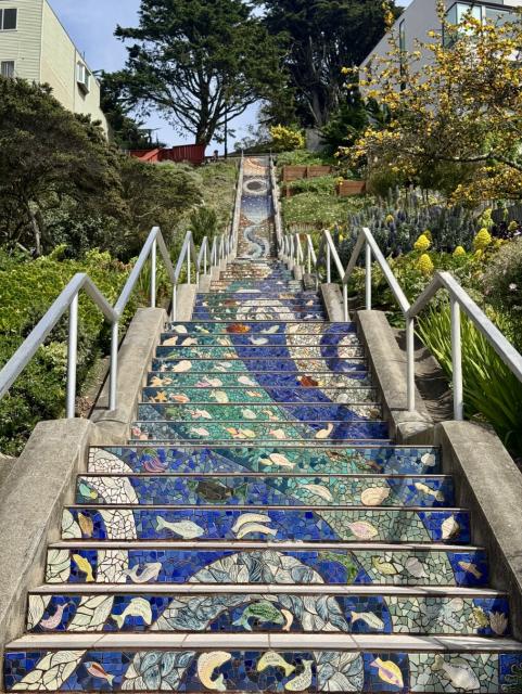 A view looking up a large flight of stairs. Tiles on the stairs' faces show fish and other natural scenes. [iPhone 15 Pro]