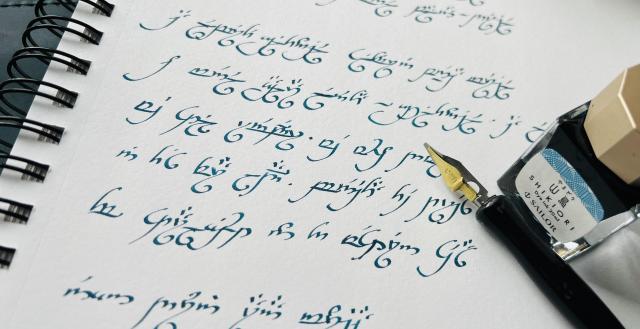 Notebook page with deep blue-green Elvish script, visibly crooked, with a bottle of ink (Sailor Shikiori – Yamadori) and a calligraphy dip pen. The poem reads:
A Elbereth Gilthoniel
Silivren penna míriel
O menel aglar elenath
Gilthoniel, a Elbereth!
We still remember, we who dwell
In this far land, beneath the trees
The starlight on the Western seas.

(I've probably left out some accents)