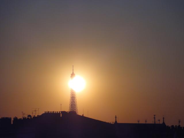 Contre-jour sur les toits de paris, on voit la tour Eiffel et le soleil qui la mange. Ca ressemble à un phare.