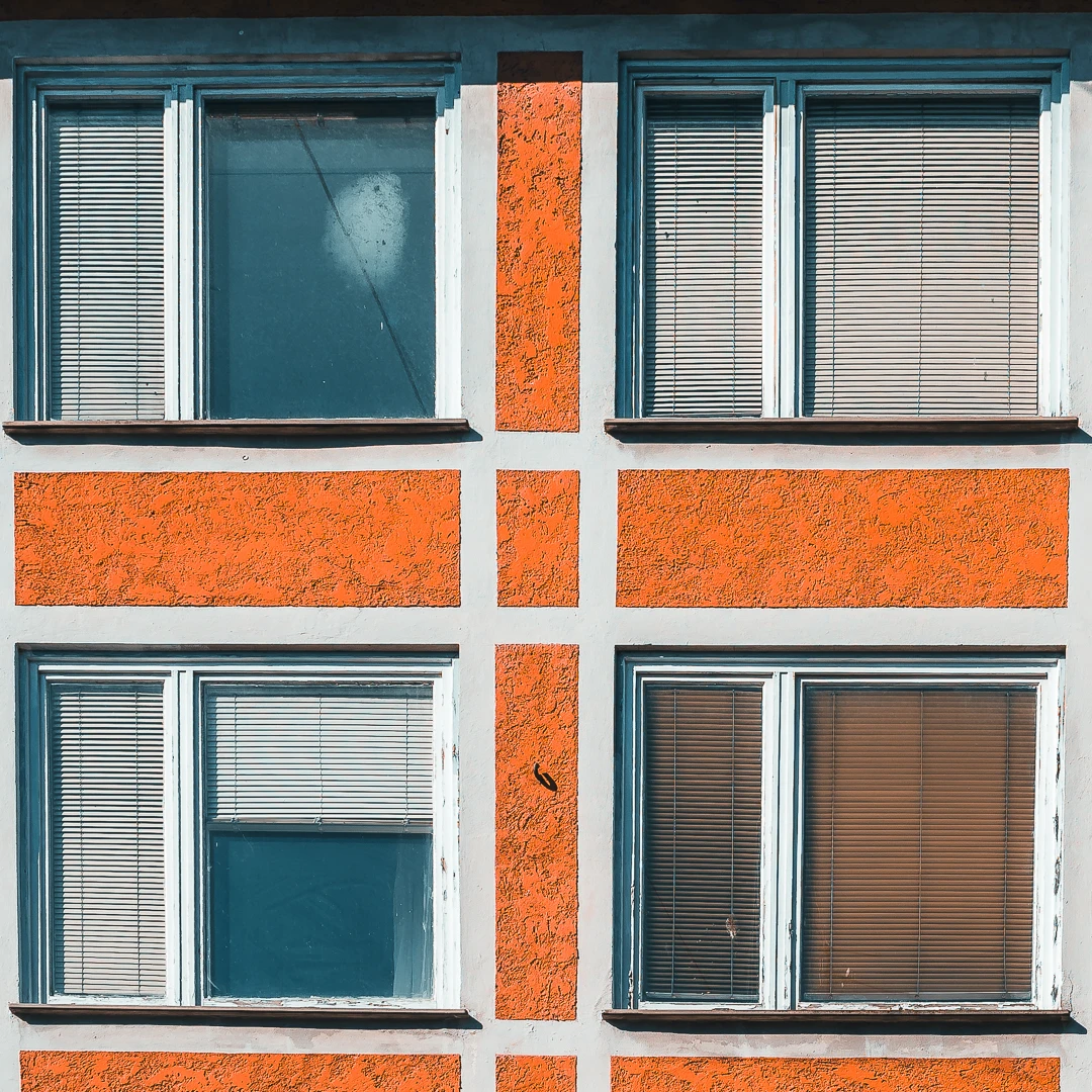 Ausschnitt einer Fassade mit vier Fenstern: zwei Reihen, zwei Zeilen. Die Rahmen sind relativ weiß, die Fassade in einem herrlichen 70er-Jahre-Orange.