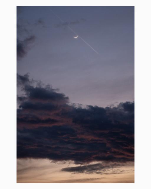 EN: A photograph of a twilight sky in portrait orientation. The image features a crescent moon and a faint contrail high above in a deep, purple-grey dusk sky. Below these, a substantial, dark cloud formation with deep crimson and magenta undersides dominates the central portion. The very bottom reveals a softer, peach and gold sunset-colored cloud layer. The photograph is clean, without graphic overlays.

DE: Fotografie eines Abendhimmels im Hochformat. Das Bild zeigt eine Mondsichel und einen schwachen Kondensstreifen hoch oben in einem tiefen, lilagrauen Himmel. Darunter dominiert eine mächtige, dunkle Wolkenformation mit tiefpurpurnen und magenta Unterseiten den mittleren Bereich. Ganz unten zeigt sich eine weichere, pfirsich- und goldfarbene Wolkenschicht in Sonnenuntergangsfarben. Das Foto ist klar und ohne grafische Überlagerungen.