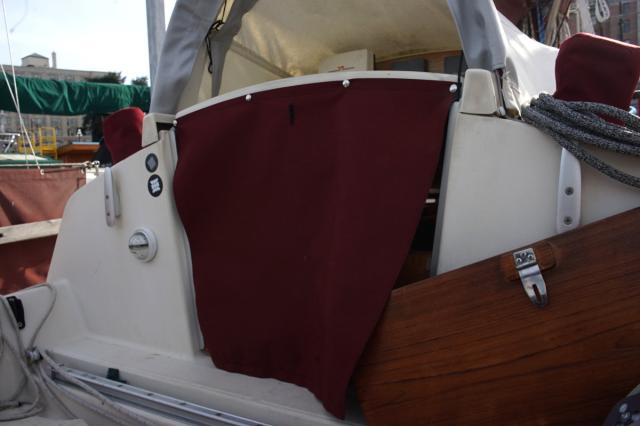 a view of the cockpit of a sailboat, showing the companionway door boards covered by a red fabic, secured by with dome fasteners.