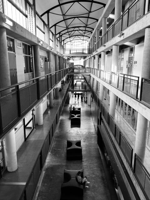 View down a large passage lined with several floors of rooms, a walkway on each floor and a curved roof above. It looks like a scene from a prison.
