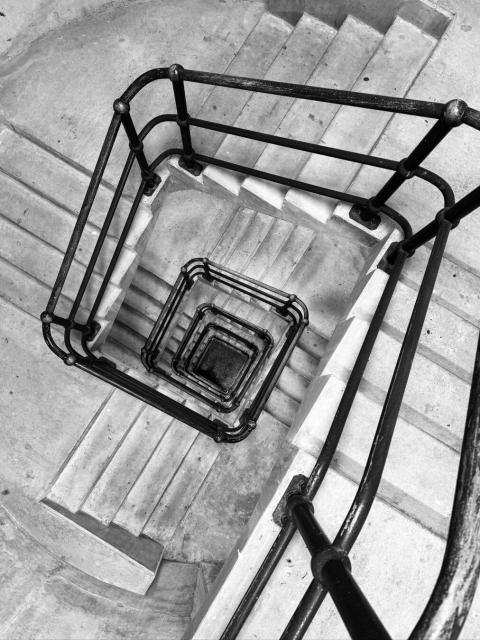 Looking down a square stairwell. The stairs are concrete and the railings metal tubing.