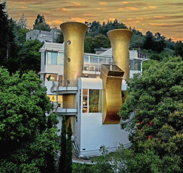 A multi-story house perched on a hillside. Its defining feature is 2 large towers shaped like golden horns, and a 3rd that is curved and squared off at the top. 