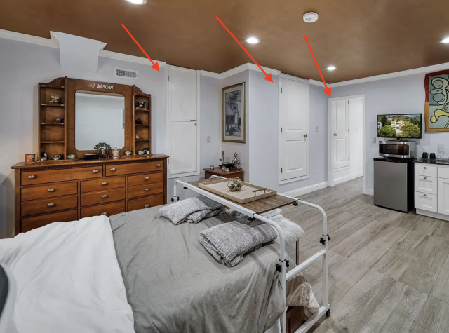 A bedroom with 2 small doors that look like they're upside down, they are about a foot off the ground and the base is actually meeting up with the ceiling. Through a door you can see a 3rd door like that. 
