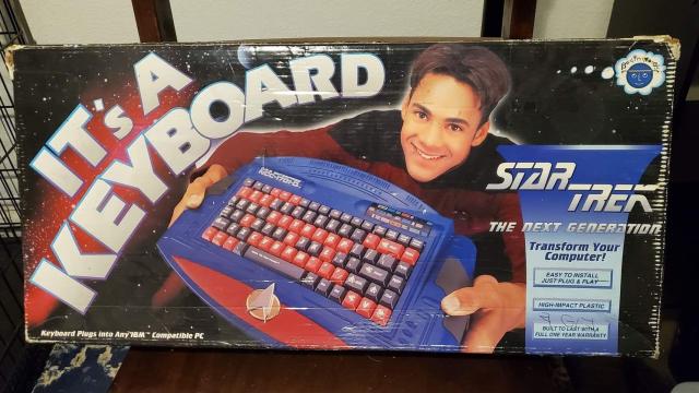 a box for a star trek TNG plastic keyboard, all blue & red, with the starfleet badge & a bit of the NCC-1701-D dish. held up by a kid who looks a bit like jake sisko with a poorly-photoshopped mushroom cut? anyway the box says, in big letters: "IT'S A KEYBOARD"