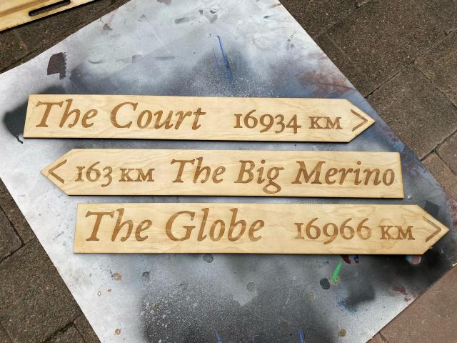 Photo of three plywood laser cut and engraved  directional signs marked “The Court - 16934km”, “163km - The Big Merino” and “The Globe - 16966km”