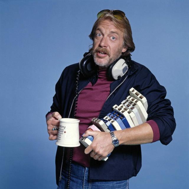 Howard Hesseman as Dr. Johnny Fever on WKRP In Cincinnati. He's holding a stack of 8-tracks, his signature coffee mug, and wearing his large headphones around his neck.