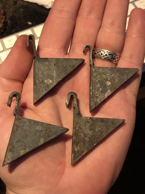 Four triangular pieces of steel with a flat hook protruding from one of the short ends at the right angle.