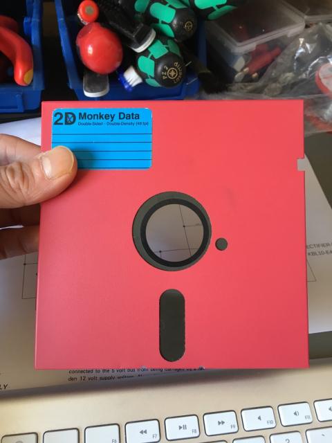 Hand holding a red 5.25 inch floppy disk with a blue label