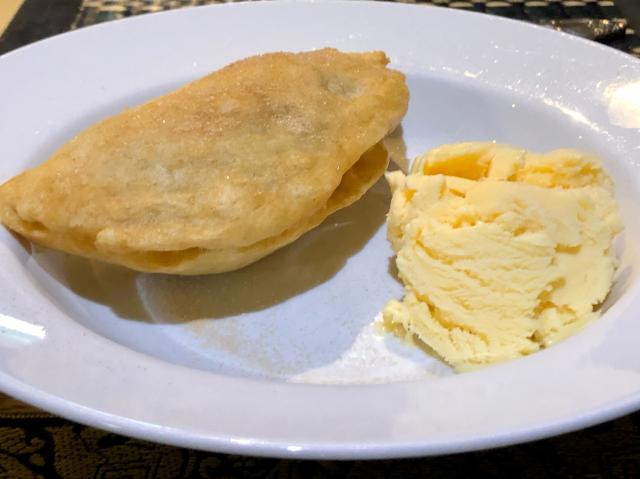 A crescent pastry filled with apple next to a scoop of icecream in a bowl. 