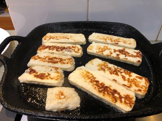 Slices of haloumi frying in a cast iron frypan