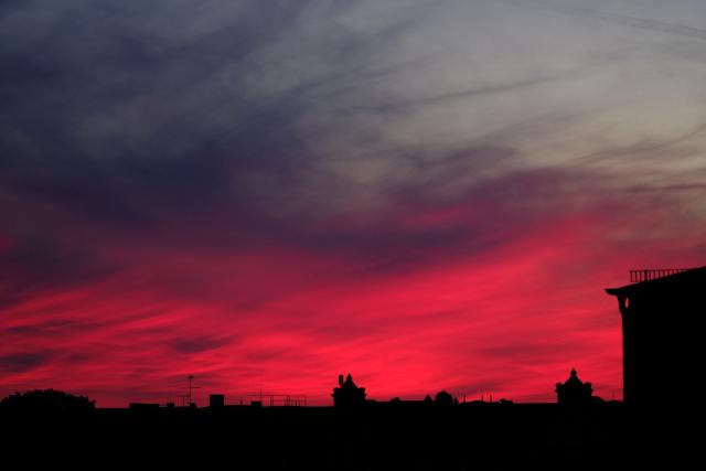 A skyline of rooftops under a dramatic evening sky with red clouds.