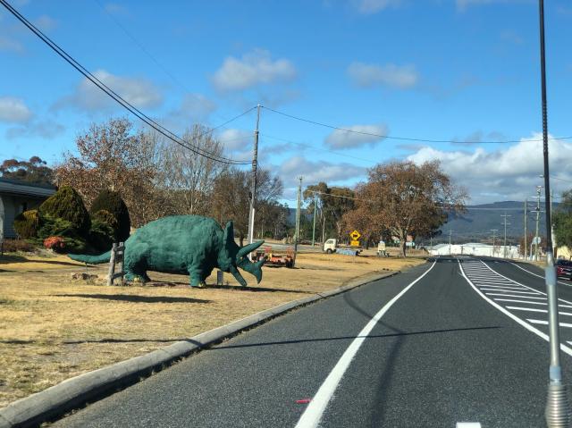 A green triceratops stands next to the highway