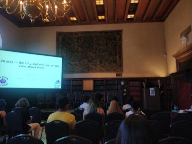 Old looking room with a speakers podium on the right and a PowerPoint on the right. The first slide has the title: "viruses in the city and why we should care about them"