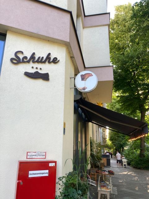 Big sign: Schuhe
Small sign: hand holding shoe by lace, but the whole picture is inverted 