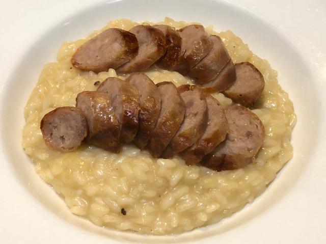 A bowl of yellow-ish risotto with sliced pork sausage on top. 