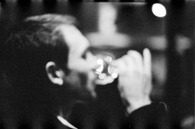 A blurry portrait of a man drinking a glass of wine.