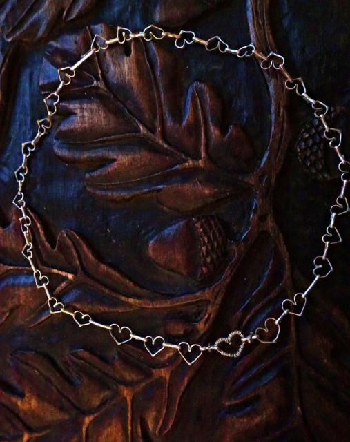 Little silver necklace /chain made of small linked hearts. It's placed on a pretty wooden box. 