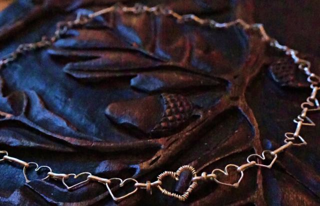 Closeup picture. There is thin wire wrapped around the heart in the middle, as well as two small rings on each side of the links between the hearts. 