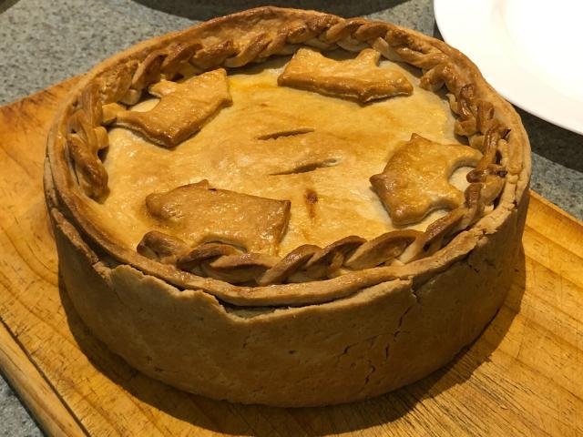 A baked standing crust pork and apple pie, decorated with pastry pigs and braiding. 
