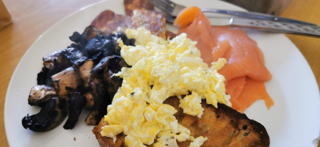 A steaming breakfast plate; toast, scrambled egg, mushrooms, fried halloumi, and smoked salmon-trout