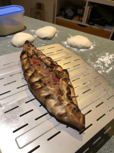 A turkish style pide on a pizza peel with three dough balls in the background. 