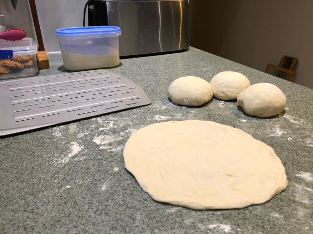 Three balls of dough and one pizza round, next to the pizza peel