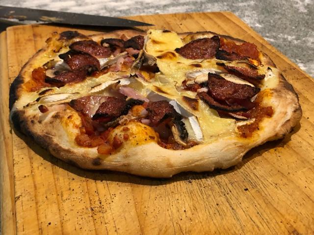 Cooked pizza. Contains bacon, mushroom, salami and camembert cheese