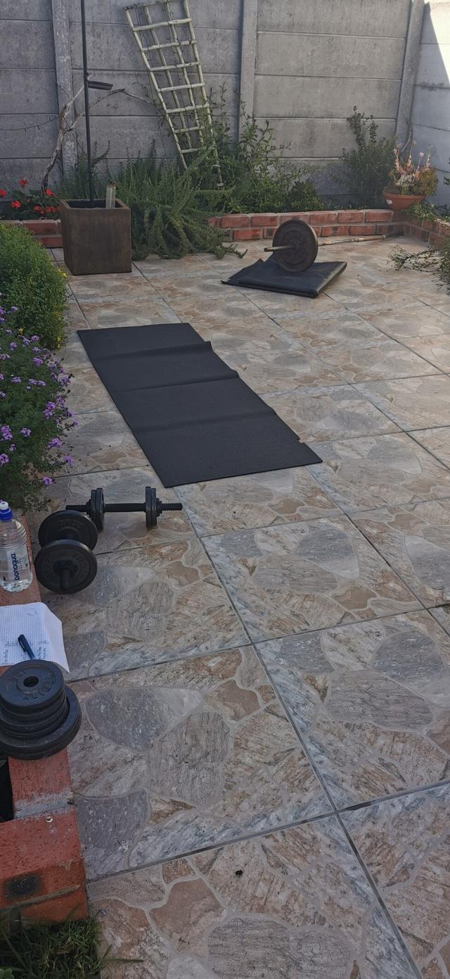 A little home gym set up on my patio, with dumbbells, a barbell, and yoga mats