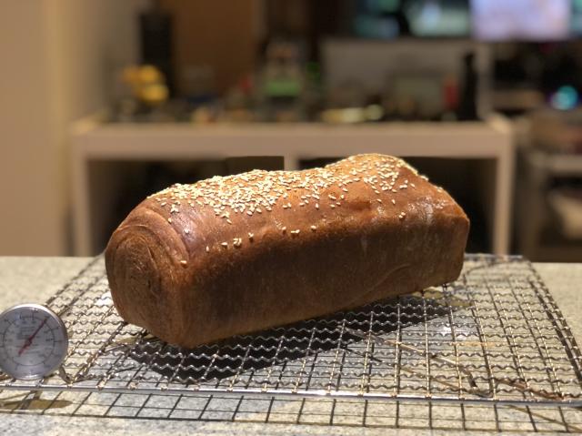 Dark, rounded top rectangular loaf on a cooling tray. The top has sesame seeds on it. 