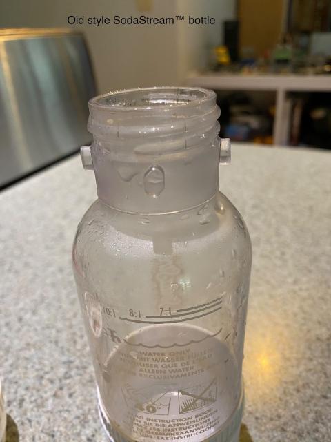 The top of an old style sodastream bottle showing the screw thread and four locking lugs below it