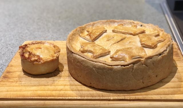 One small pie next to a large standing crust pie with pasty pigs on top. 