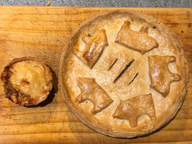 Top down view of a small pie on the left and large pie with pastry pigs on top on the right