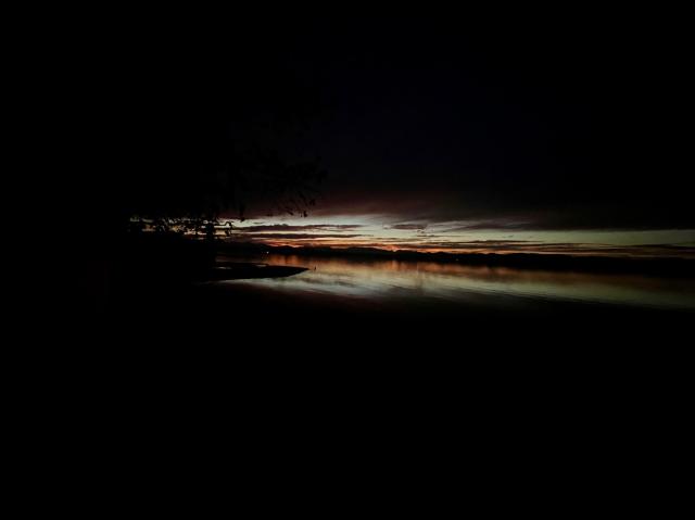 Sundown on Lake Champlain, Vermont. Black sky and black water, a band of light, the waning sunset, in the center.