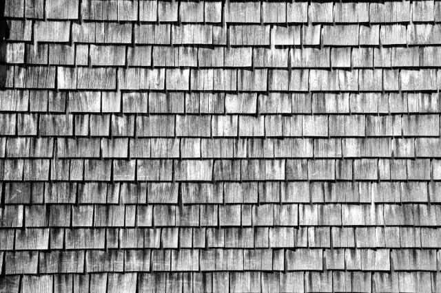 Schwarz-Weiß Bild der Holzfassade an einer Hütte in den Alpen. Sieht toll die Färbung und Struktur der Holzschindeln mit denen die Fassade der Hütte bedeckt ist.