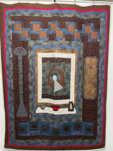 This is a Star Trek Vulcan Tapestry quilt. The IDIC symbol is in the center. A plaque with Vulcan writing is on the right. A Vulcan Lyre is appliquéd on the left. 