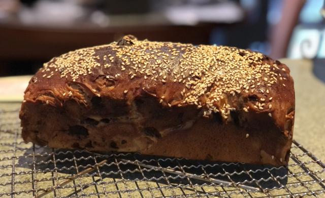 A dark brown fruit loaf topped with a generous amount of sesame seeds 