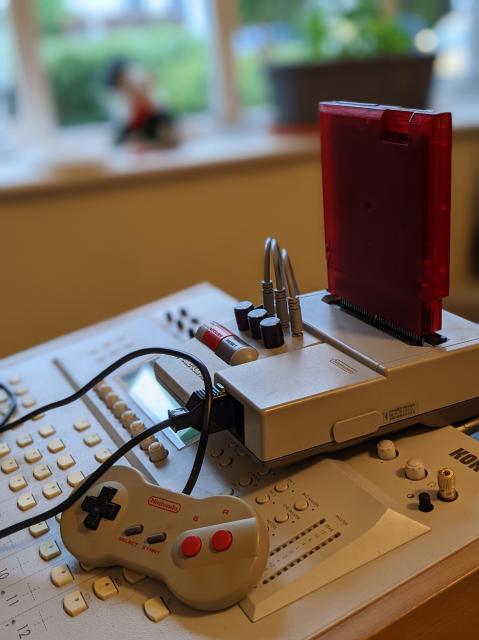 Famicom AV with a Powerpak cartridge plugged in, sitting atop a Korg 168RC mixer. Three mini-jack cables are connecting from the Famicom to the mixer.