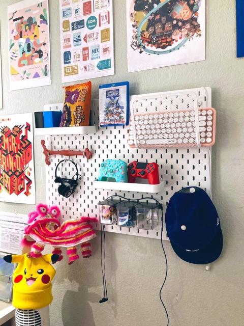 IKEA pegboard with an assortment of items on it; Dodgers hat, two controllers, keyboard, Chinese Dragon puppet, headphones, and Pokemon cards