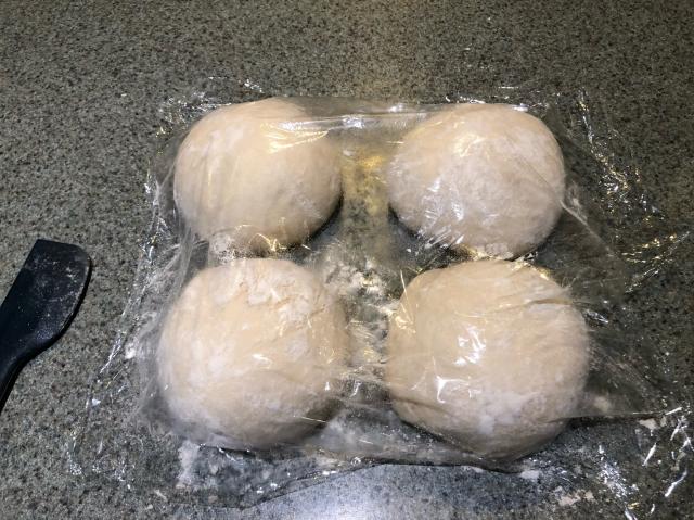Four balls of pizza dough under some plastic wrap