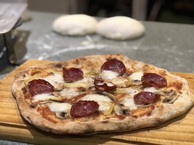 A pizza on a board with dough in the background. 