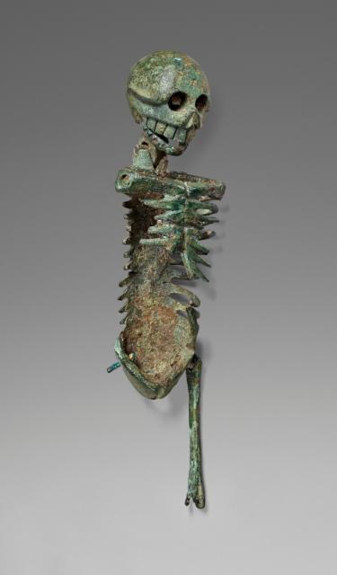 Slight side view of a small bronze articulated skeleton, missing its arms and a leg. It has a green patina throughout