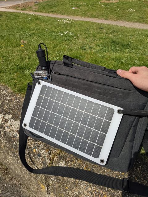 Shoulder bag with a solar panel cover most of the outside surface. A small LCD multimeter is visible connected to it.