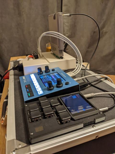 Music equipment cabled together. Closest to camera is a M8, next is a 1010Music Bluebox, and finally a Famicom AV with a MIDINES cartridge and three audio outputs connected to the Bluebox.