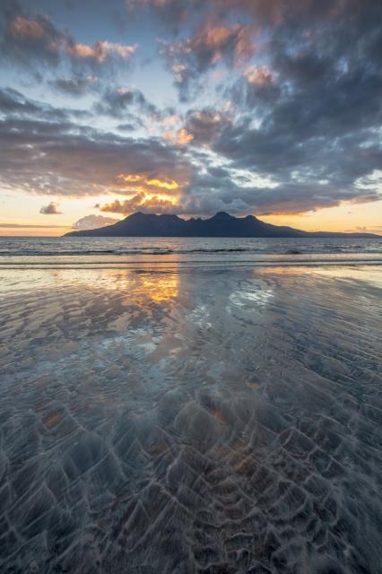 The Scottish Island of Rum seen from Laig Beach on the island of Eigg. The sunset is reflected in the wet sand.