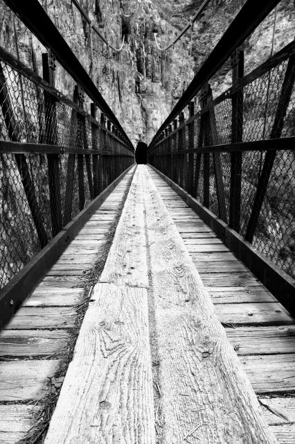 Black and white photo, taken low,  suspension foot bridge for hikers across the Colorado river in Grand Canyon, USA